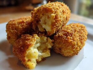 Close-up of crispy, golden brown potato croquettes, one broken open showing the soft, cheesy interior.