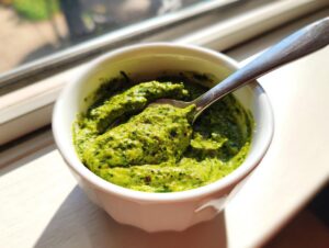 A vibrant green, textured dip, possibly pesto or herb-based, served in a small white bowl with a spoon, next to a sunny window, despite the article being about black bean dip.