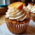 Close-up of a Honey Peach Cream Cheese Cupcake topped with white frosting, sliced peaches, and a honey drizzle.