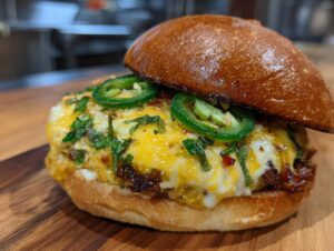 A close-up of a delicious Jalapeno Popper Smash Burger, topped with melted cheese, fresh jalapenos, and herbs.