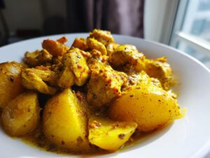 Close-up of vibrant yellow Jamaican curry chicken pieces mixed with large chunks of potato in a white bowl.