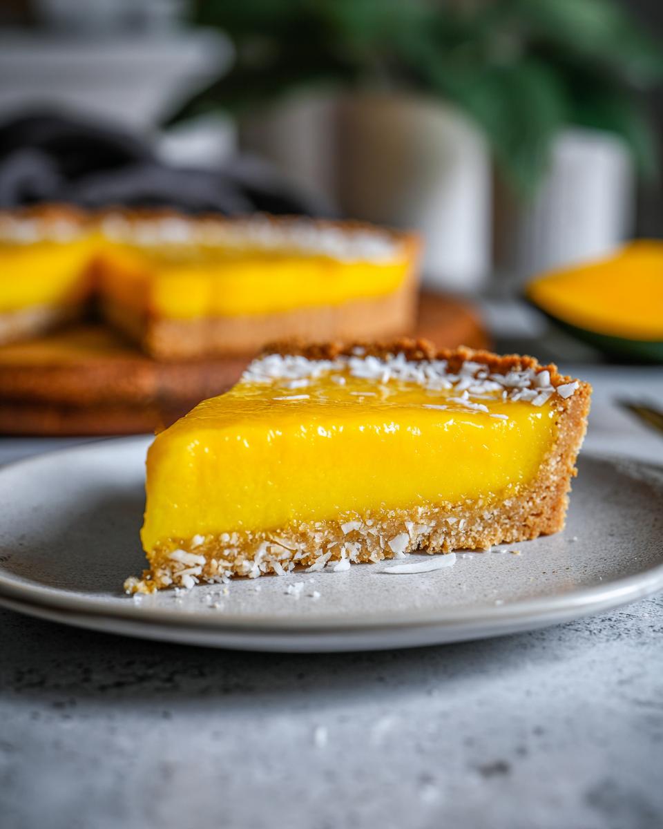 A close-up of a slice of mango curd tart, topped with shredded coconut, on a grey plate.