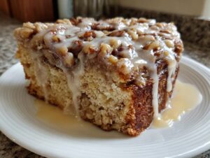 A moist slice of maple walnut coffee cake with a glaze and chopped walnuts on top, served on a white plate.