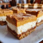 Close-up of a layered pumpkin cheesecake bar with a graham cracker crust and creamy filling.