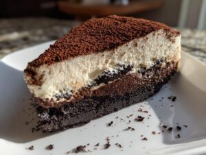A decadent slice of tiramisu cheesecake showing layers of dark chocolate crust, creamy filling, and a thick cocoa powder topping.