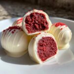 Close-up of white chocolate coated red velvet cake pops, one cut in half showing the rich red interior.