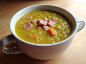 Close-up of a thick, yellow-green bowl of pea soup topped with diced ham and carrots.