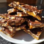 A stack of broken pieces of homemade almond chocolate toffee recipe on a white plate.