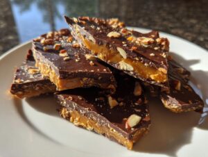 Close-up of broken pieces of chocolate-covered toffee recipe snap topped with chopped nuts on a white plate.