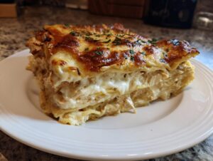 A rich, layered slice of chicken lasagna with a golden-brown, cheesy top sprinkled with parsley.