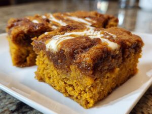Two squares of moist pumpkin dump cake with a swirled cream cheese topping on a white plate.