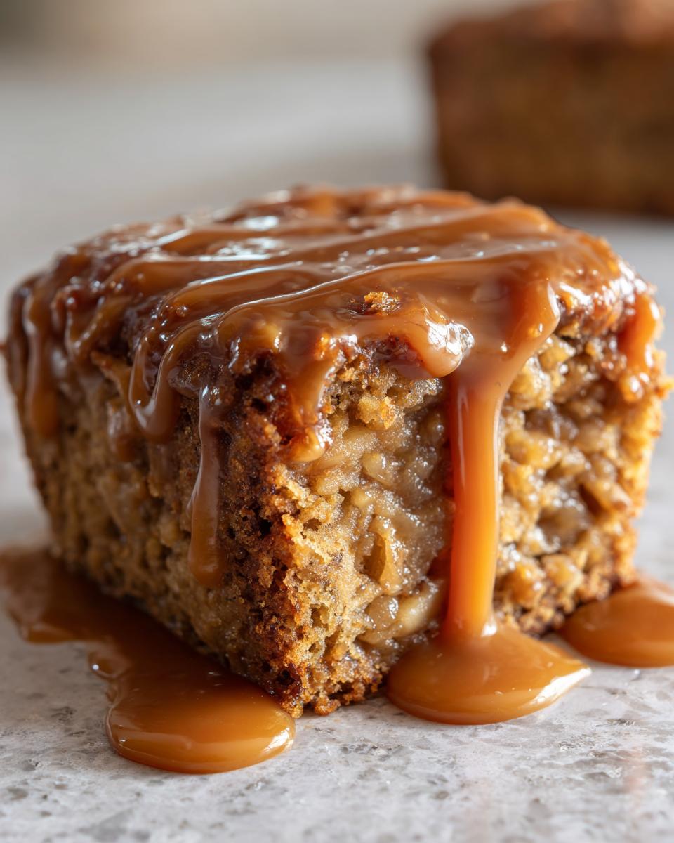 Close-up of a moist slice of apple bread pudding generously topped with warm caramel sauce.