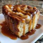 Close-up of a single serving of apple bread pudding topped generously with thick caramel sauce.