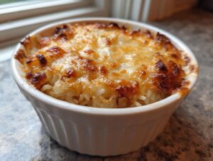 Close-up of baked french onion butter rice topped with bubbly, browned, melted cheese in a white ceramic ramekin.