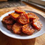 Close-up of glistening, glazed slices of candied sweet potatoes piled on a white plate.