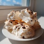 A stack of light, airy, slightly browned forgotten cookies topped with mini chocolate chips on a white plate.