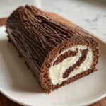 A close-up of a slice of chocolate yule log cake showing the dark chocolate sponge rolled around a white cream filling.