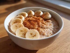 A white bowl filled with creamy banana oatmeal, topped with sliced bananas and a dusting of cinnamon.