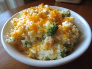 A close-up of a creamy broccoli and rice casserole topped with melted cheddar cheese in a white bowl.