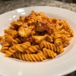 Close-up of creamy cajun chicken pasta with rotini noodles and seasoned chicken pieces in a white bowl.