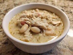 Close-up of a white bowl filled with creamy chicken chili, featuring shredded chicken and white beans.