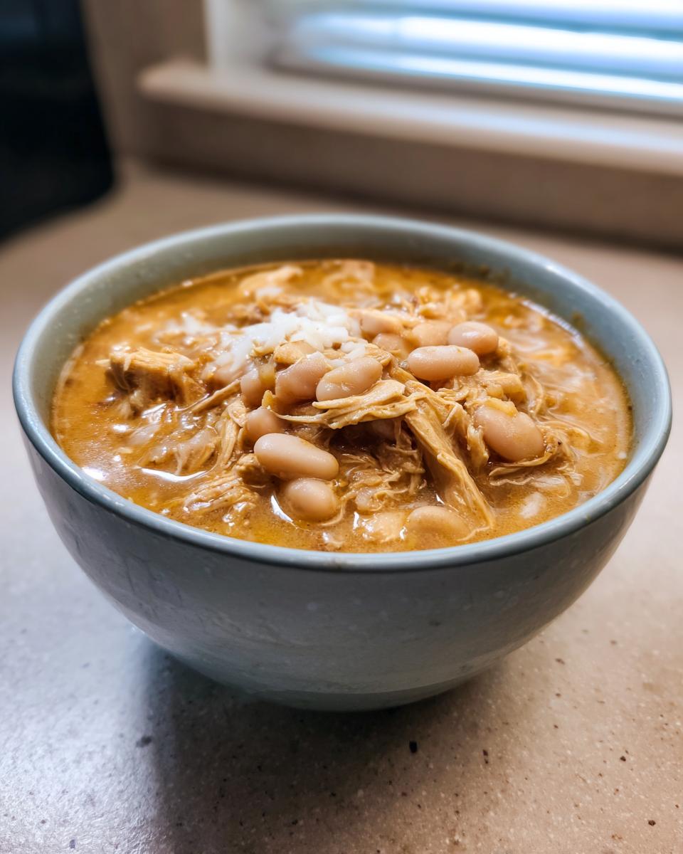 A close-up of a light blue bowl filled with creamy chicken chili, featuring shredded chicken and white beans.