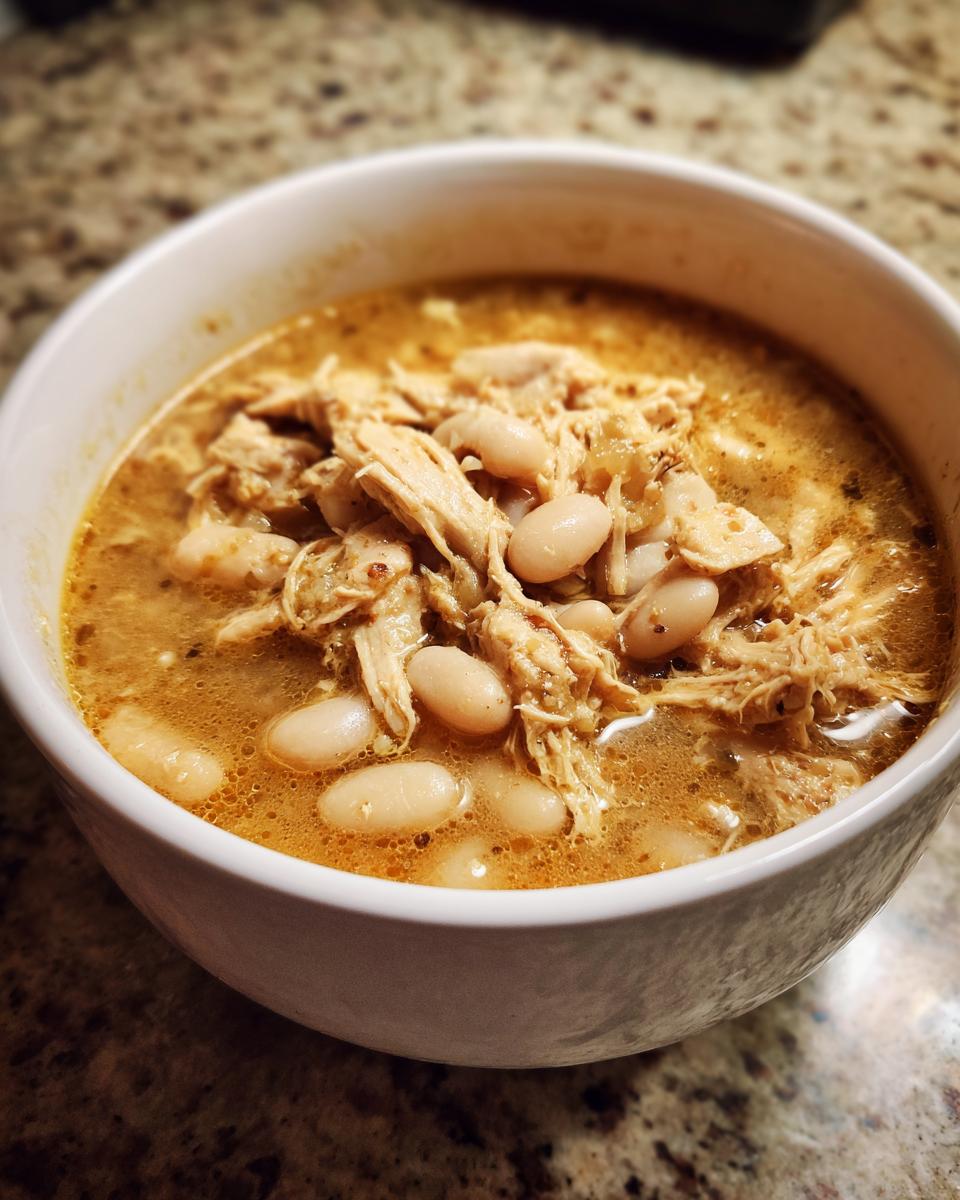 Close-up of a white bowl filled with creamy chicken chili, featuring shredded chicken and white beans in a rich broth.