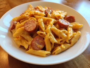 A close-up of creamy kielbasa pasta made with penne pasta and sliced smoked sausage on a white plate.