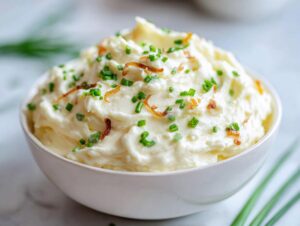 A bowl of creamy, fluffy onion dip garnished with fresh green chives and crispy fried onions.