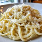 Close-up of creamy spaghetti tossed in sauce and heavily topped with grated parmesan pasta.