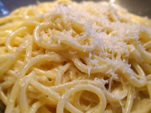 Close-up of creamy spaghetti noodles coated in sauce and topped with freshly grated parmesan pasta.