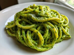A mound of thick pasta coated richly in bright green creamy pesto pasta, topped with grated cheese.