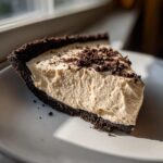 A thick slice of no-bake peanut butter pie with a dark chocolate crust, served on a white plate.