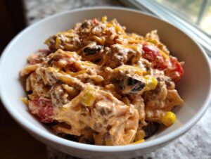 Close-up of a creamy taco pasta salad featuring ground meat, cheese, corn, and black olives in a white bowl.