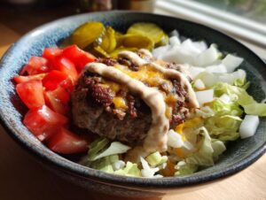 A close-up of a delicious cheeseburger bowl featuring a cheesy patty, lettuce, tomatoes, onions, pickles, and special sauce.