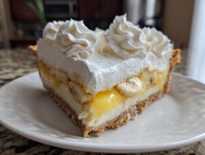 A perfect slice of banana cream pie showing layers of crust, cream, banana slices, and whipped topping.
