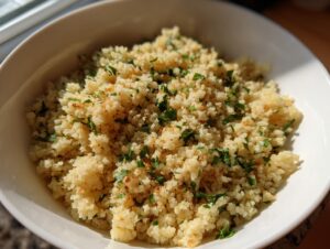 A close-up of fluffy, seasoned cauliflower rice garnished with chopped green herbs in a white serving bowl.