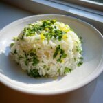 A mound of fluffy cilantro lime rice garnished generously with chopped cilantro and bright yellow lime zest.