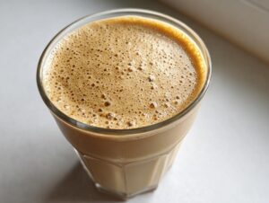 Overhead close-up of a freshly blended peanut butter banana smoothie with a thick layer of light brown foam.