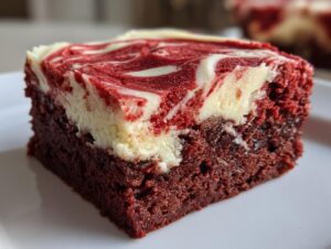 Close-up of a fudgy red velvet brownie square topped with a white and red cream cheese swirl.