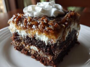 Close-up of a slice of german chocolate poke cake showing dark chocolate layers, white filling, and pecan coconut topping with whipped cream.