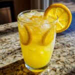A tall, sweating glass filled with bright yellow homemade lemonade, crushed ice, and lemon slices.