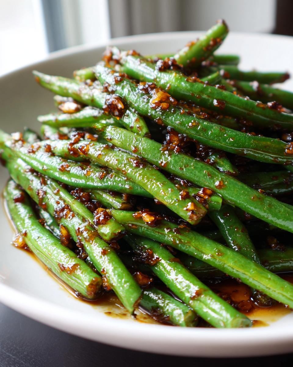 Close-up of bright green beans tossed in a savory, dark garlic sauce.