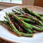 Close-up of vibrant green beans coated in a rich, dark, savory glaze.