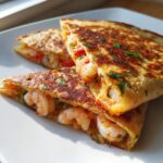 Close-up of three golden-brown, folded shrimp quesadilla wedges filled with plump shrimp and tomatoes.