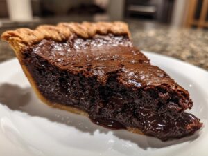Close-up of a slice of hot fudge pie showing the rich, gooey chocolate filling oozing out onto a white plate.