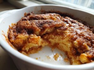 Close-up of a freshly baked snickerdoodle cobbler with a gooey, cinnamon-sugar topping in a white dish.