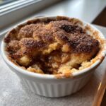 Close-up of a warm snickerdoodle cobbler with a cinnamon-sugar topping served in a white ramekin.