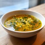 Close-up of a warm bowl of golden pastina soup topped with fresh parsley.