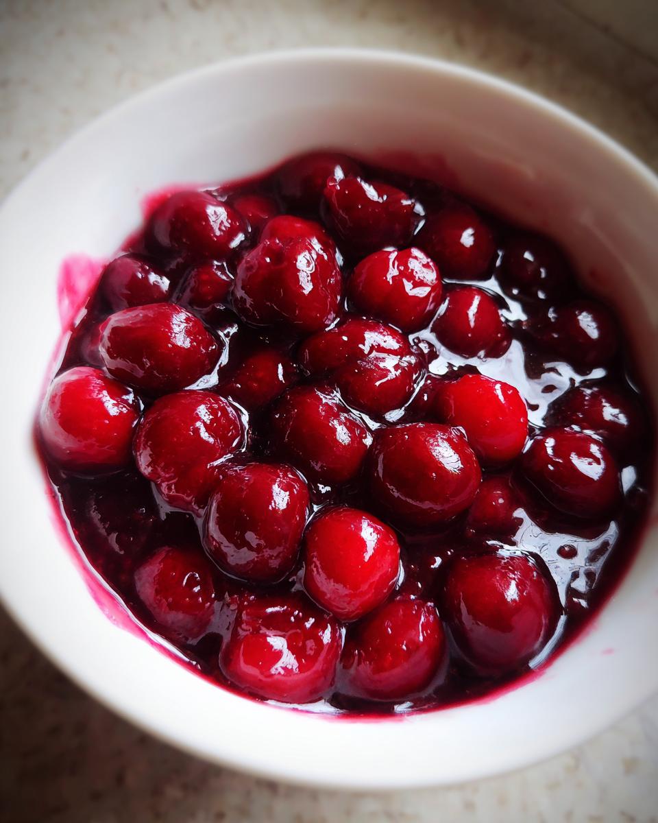 Close-up of glossy, deep red cherries suspended in thick sauce, ready to be used as cherry pie filling.